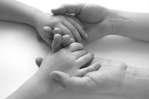 Black and white image of a person holding a baby hand