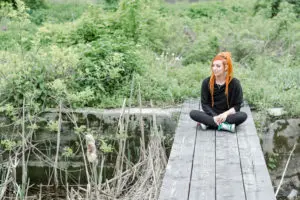 A girl with orange hairs sitting on a wooden bridge