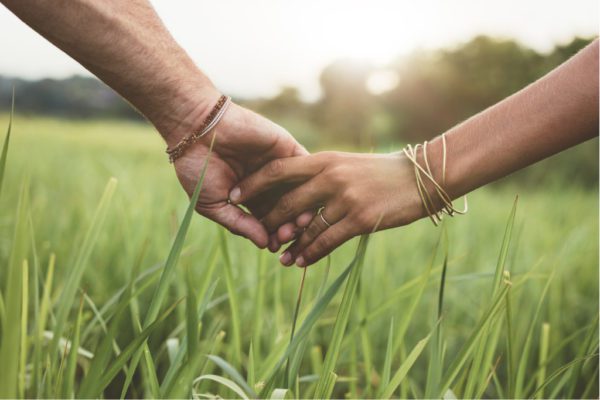 Two hands holding each other in a green field