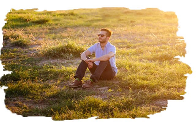 photo of a man sitting in a field wearing sunglasses looking into the distance